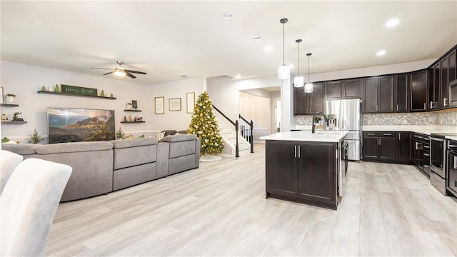 kitchen with ceiling fan, tasteful backsplash, pendant lighting, a center island with sink, and light wood-type flooring