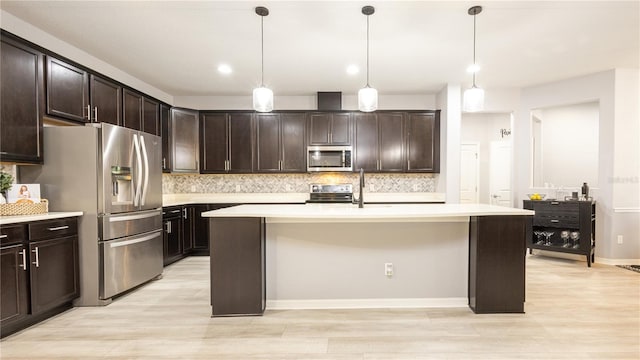 kitchen with decorative light fixtures, dark brown cabinetry, a kitchen island with sink, and appliances with stainless steel finishes