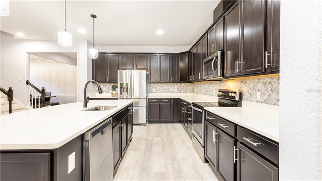 kitchen featuring hanging light fixtures, sink, light hardwood / wood-style flooring, an island with sink, and stainless steel appliances