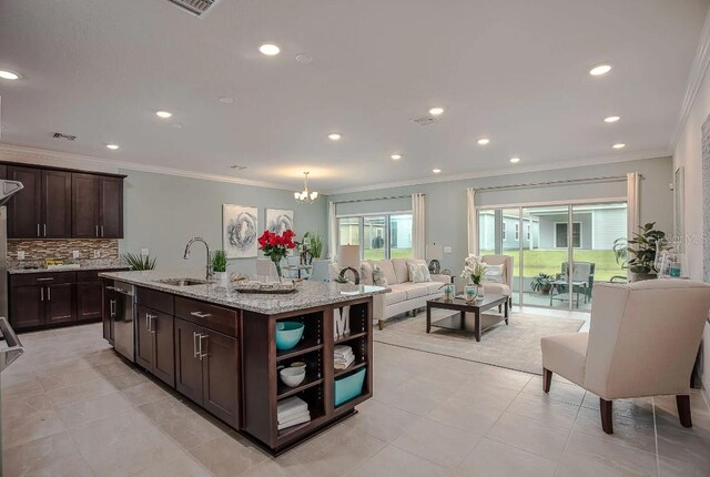 kitchen with backsplash, sink, light stone countertops, an island with sink, and dark brown cabinetry