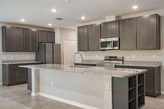 kitchen featuring appliances with stainless steel finishes, dark brown cabinetry, a center island with sink, and sink