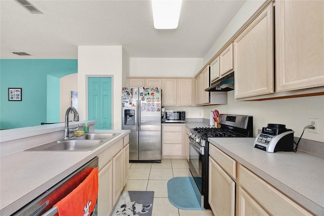 kitchen featuring sink, a textured ceiling, light brown cabinetry, light tile patterned flooring, and appliances with stainless steel finishes