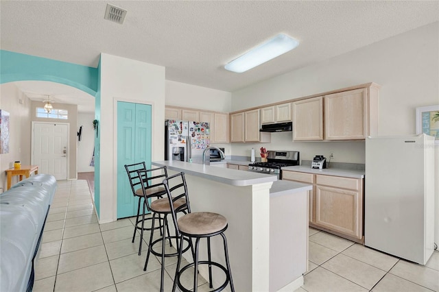 kitchen with light brown cabinetry, a textured ceiling, stainless steel appliances, and an island with sink