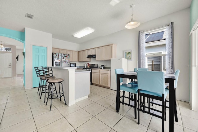 kitchen featuring decorative light fixtures, light brown cabinetry, stainless steel appliances, and a textured ceiling