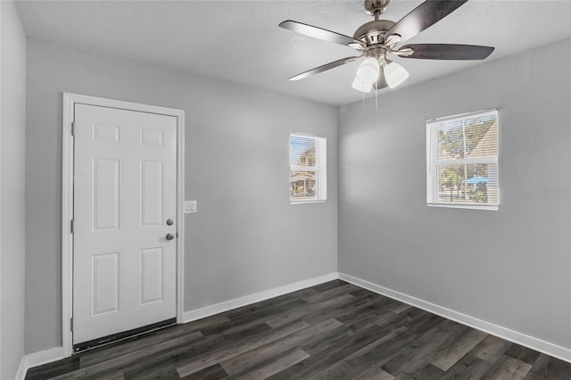 empty room featuring ceiling fan, a healthy amount of sunlight, and dark wood-type flooring