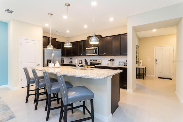 kitchen with a breakfast bar, stainless steel appliances, a kitchen island with sink, sink, and decorative light fixtures