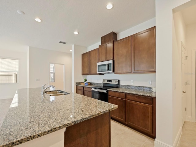 kitchen with a wealth of natural light, light stone counters, sink, and appliances with stainless steel finishes