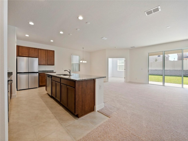 kitchen with light carpet, appliances with stainless steel finishes, a kitchen island with sink, sink, and hanging light fixtures