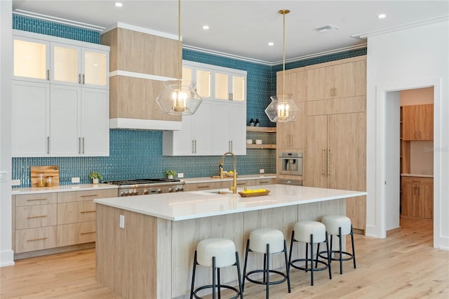 kitchen with ornamental molding, light countertops, white cabinets, and a kitchen island with sink