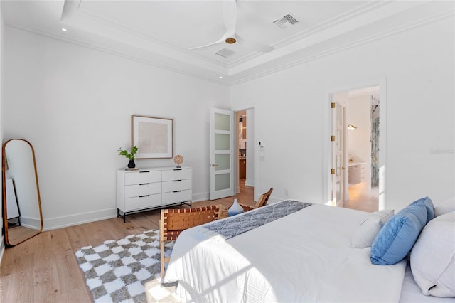 bedroom with light wood-style flooring, visible vents, baseboards, a tray ceiling, and crown molding