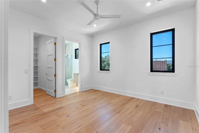 unfurnished bedroom with light wood finished floors, baseboards, ornamental molding, and a walk in closet