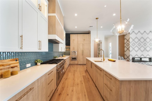 kitchen with light countertops, appliances with stainless steel finishes, a sink, and decorative light fixtures