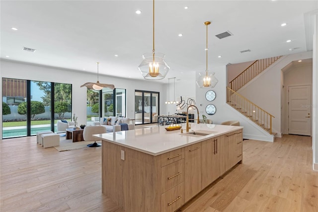 kitchen featuring visible vents, open floor plan, light countertops, a large island with sink, and a sink