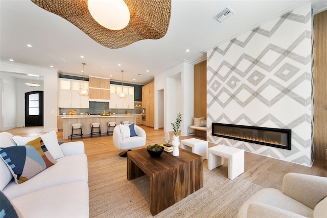 living area featuring visible vents, ornamental molding, light wood-type flooring, a fireplace, and recessed lighting