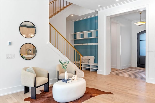 sitting room with arched walkways, stairway, ornamental molding, wood finished floors, and baseboards