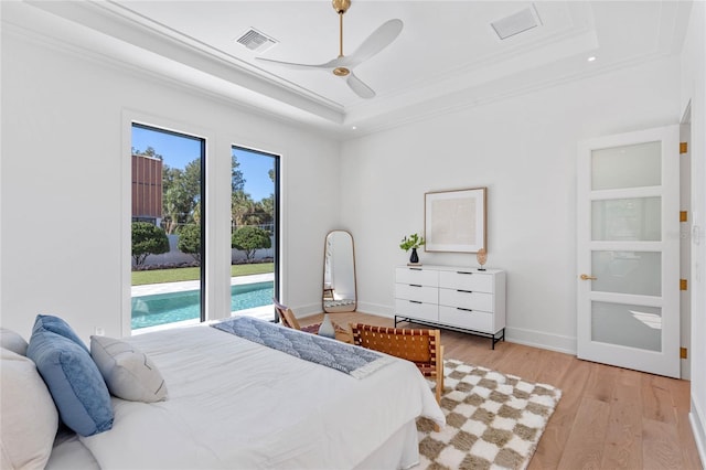 bedroom featuring baseboards, visible vents, ornamental molding, a tray ceiling, and light wood-type flooring