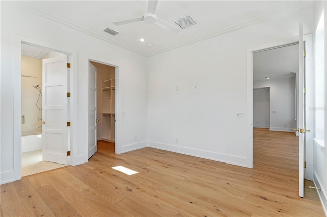 unfurnished bedroom with ornamental molding, a spacious closet, light wood-style flooring, and visible vents