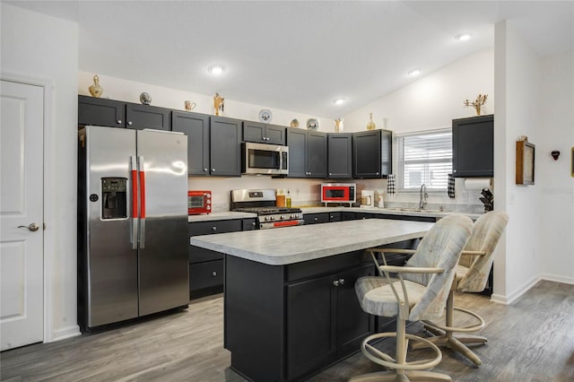 kitchen with a kitchen breakfast bar, light wood-type flooring, stainless steel appliances, vaulted ceiling, and a center island