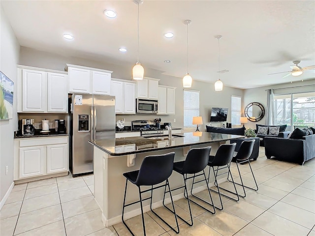 kitchen with a kitchen island with sink, a kitchen breakfast bar, ceiling fan, white cabinetry, and stainless steel appliances