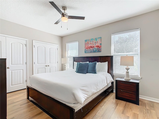 bedroom featuring a textured ceiling, light hardwood / wood-style flooring, ceiling fan, and multiple closets