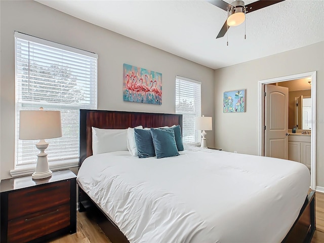 bedroom with connected bathroom, multiple windows, ceiling fan, and light hardwood / wood-style flooring