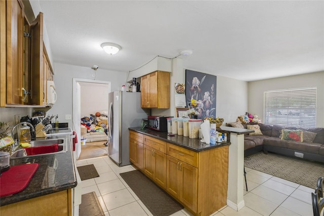 kitchen with stainless steel fridge, dark stone counters, sink, a breakfast bar area, and light tile patterned flooring