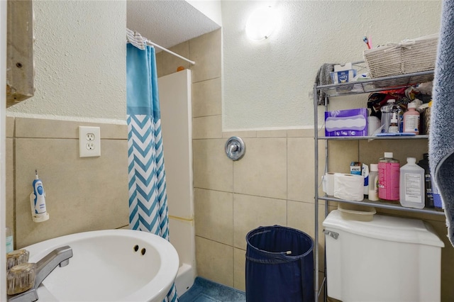 bathroom featuring a textured ceiling, toilet, and tile walls