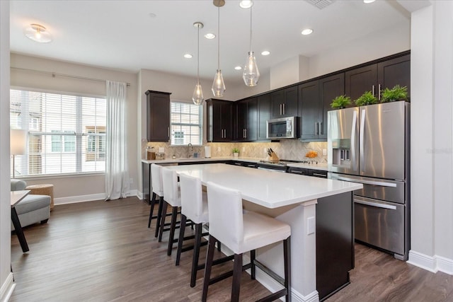 kitchen with dark wood-type flooring, hanging light fixtures, tasteful backsplash, a kitchen island, and stainless steel appliances