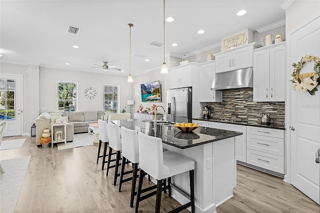 kitchen featuring pendant lighting, a breakfast bar, a center island with sink, ceiling fan, and stainless steel fridge