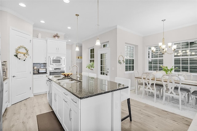 kitchen featuring a center island with sink, white cabinets, sink, and dark stone counters