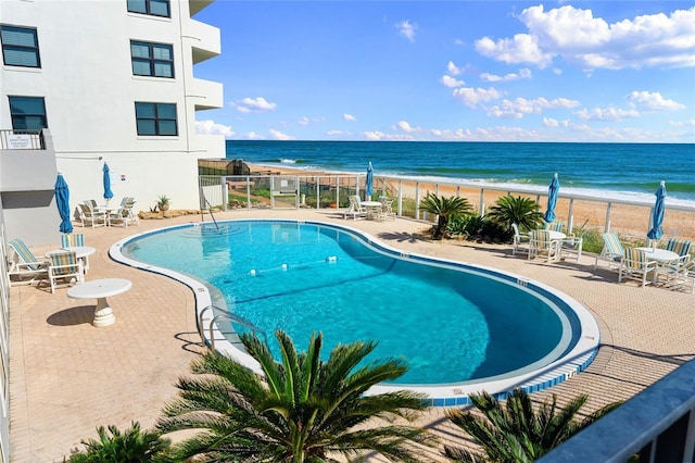 view of swimming pool featuring a patio area, a water view, and a beach view