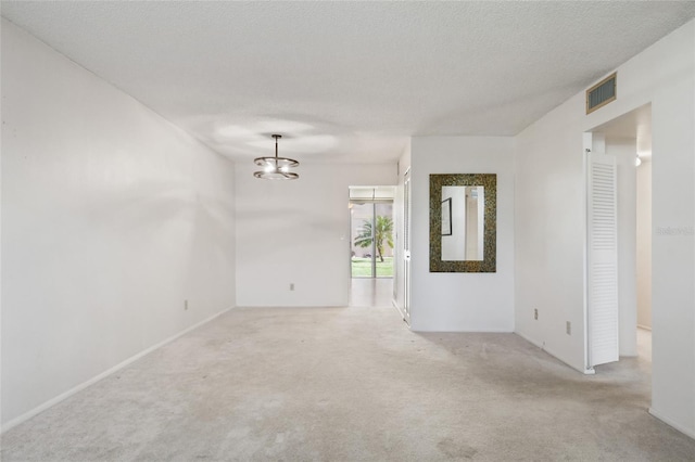 carpeted spare room with a textured ceiling and an inviting chandelier