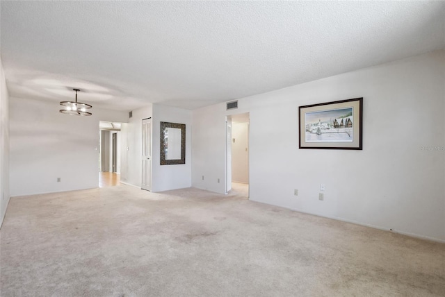 carpeted spare room with a textured ceiling and an inviting chandelier