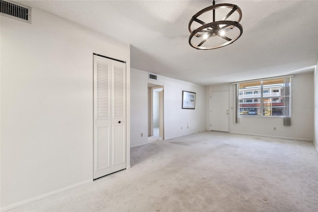 unfurnished room featuring a textured ceiling, light colored carpet, and a notable chandelier