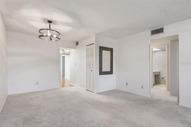 carpeted spare room featuring a chandelier and a textured ceiling