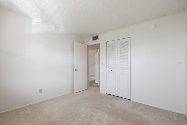 unfurnished bedroom featuring a textured ceiling, light colored carpet, and a closet