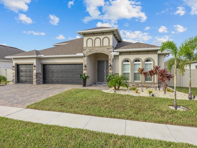 mediterranean / spanish-style home featuring a front lawn, stucco siding, decorative driveway, a garage, and stone siding