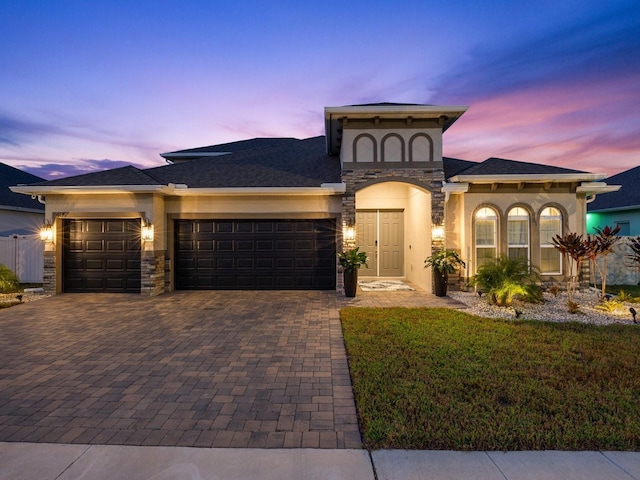 view of front facade with a garage, stone siding, decorative driveway, a front yard, and stucco siding