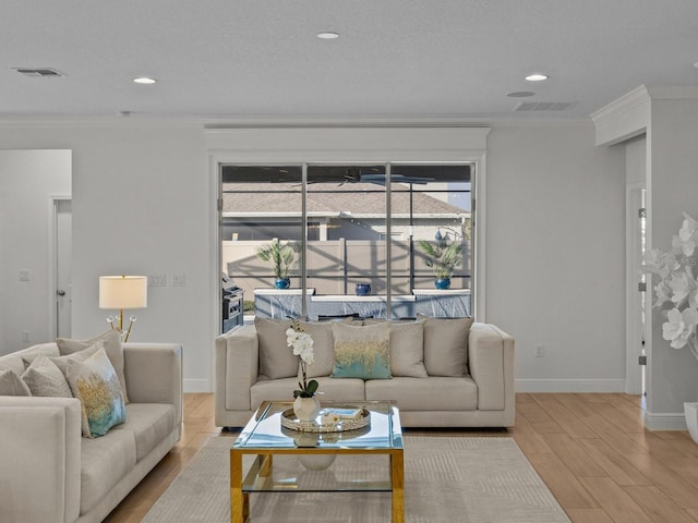 living area with visible vents, wood finished floors, and ornamental molding