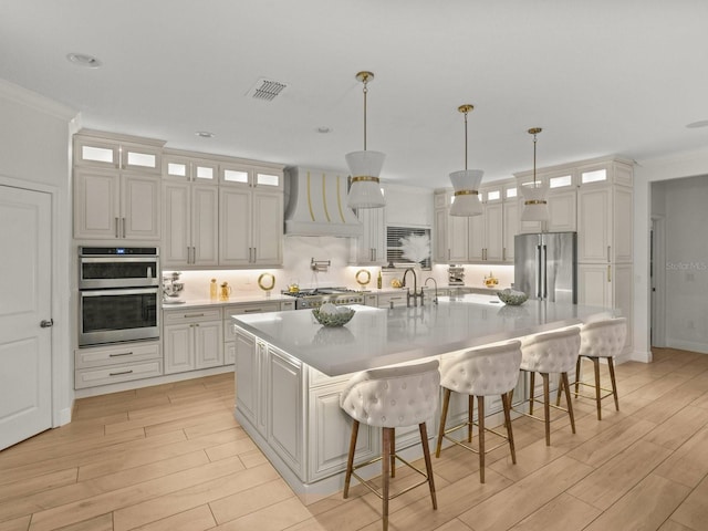 kitchen featuring wood finish floors, visible vents, custom range hood, a kitchen breakfast bar, and stainless steel appliances