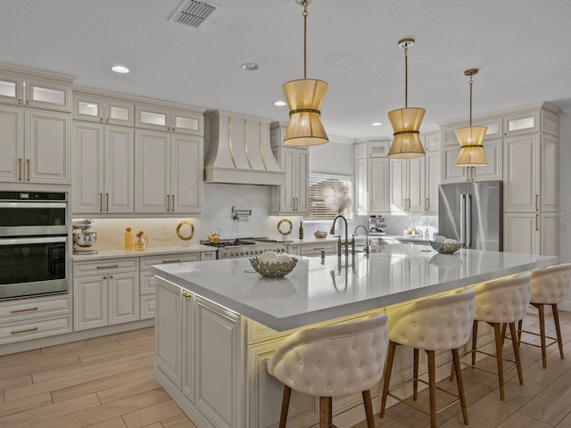 kitchen featuring visible vents, glass insert cabinets, custom exhaust hood, and appliances with stainless steel finishes