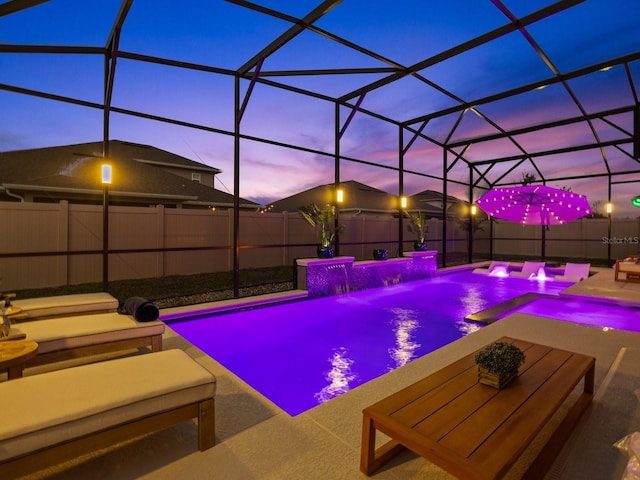 pool at dusk with glass enclosure, a fenced in pool, a fenced backyard, and a patio area