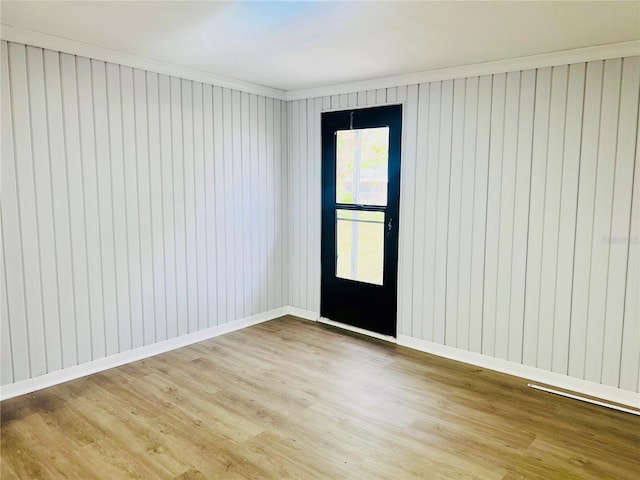 unfurnished room featuring wood walls, crown molding, and light hardwood / wood-style flooring