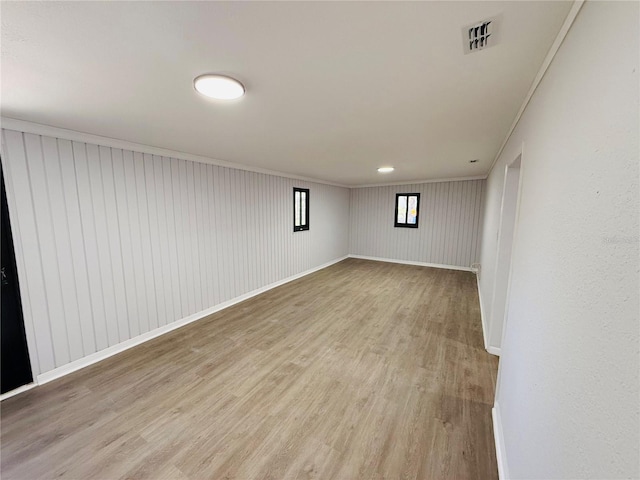 empty room with light hardwood / wood-style floors, crown molding, and wood walls