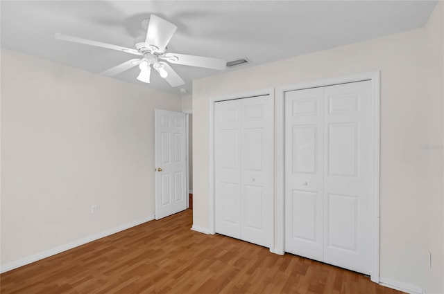 unfurnished bedroom featuring wood-type flooring, two closets, and ceiling fan