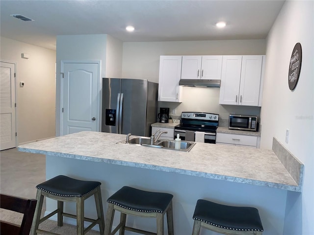 kitchen with a kitchen bar, appliances with stainless steel finishes, concrete flooring, sink, and white cabinetry