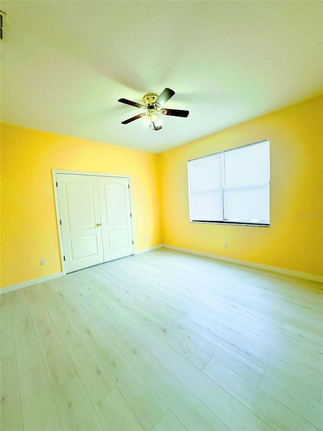 unfurnished bedroom with a textured ceiling, a closet, light hardwood / wood-style floors, and ceiling fan