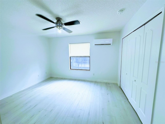 unfurnished bedroom featuring a wall mounted AC, ceiling fan, light hardwood / wood-style floors, and a textured ceiling