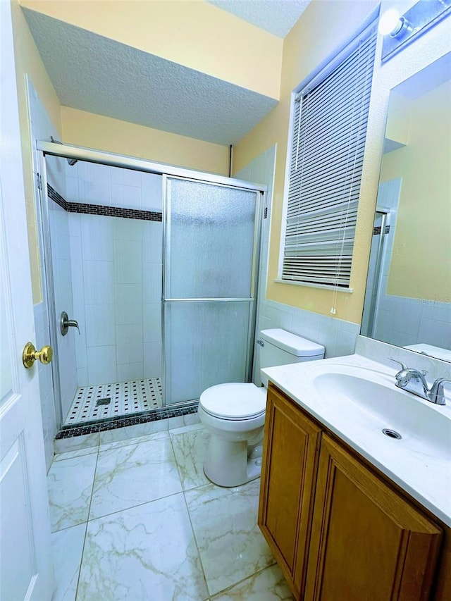 bathroom with vanity, toilet, a shower with door, and a textured ceiling