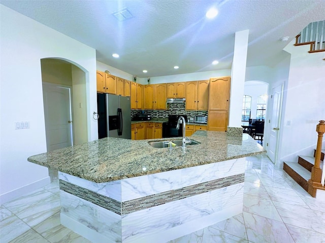 kitchen featuring kitchen peninsula, stainless steel refrigerator with ice dispenser, backsplash, a textured ceiling, and sink